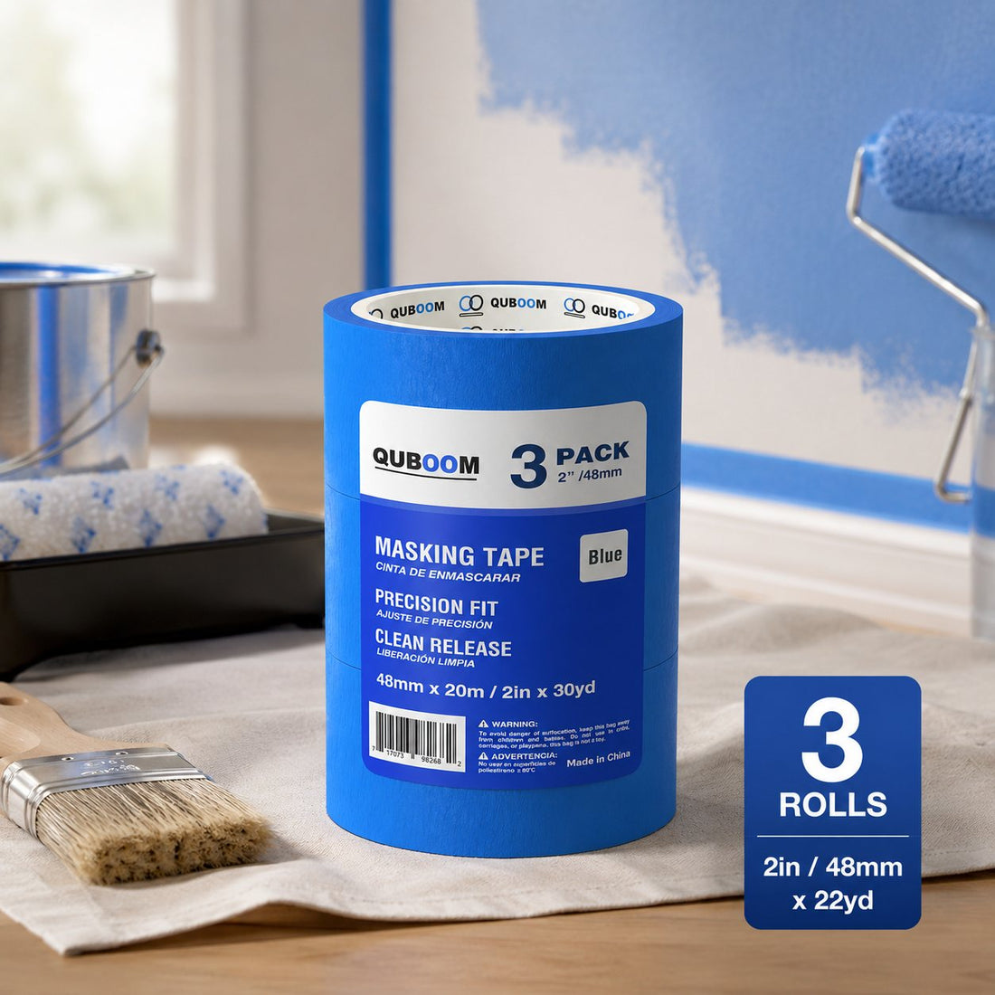 A roll of blue tape on a drop cloth in front of a wall with a paint roller