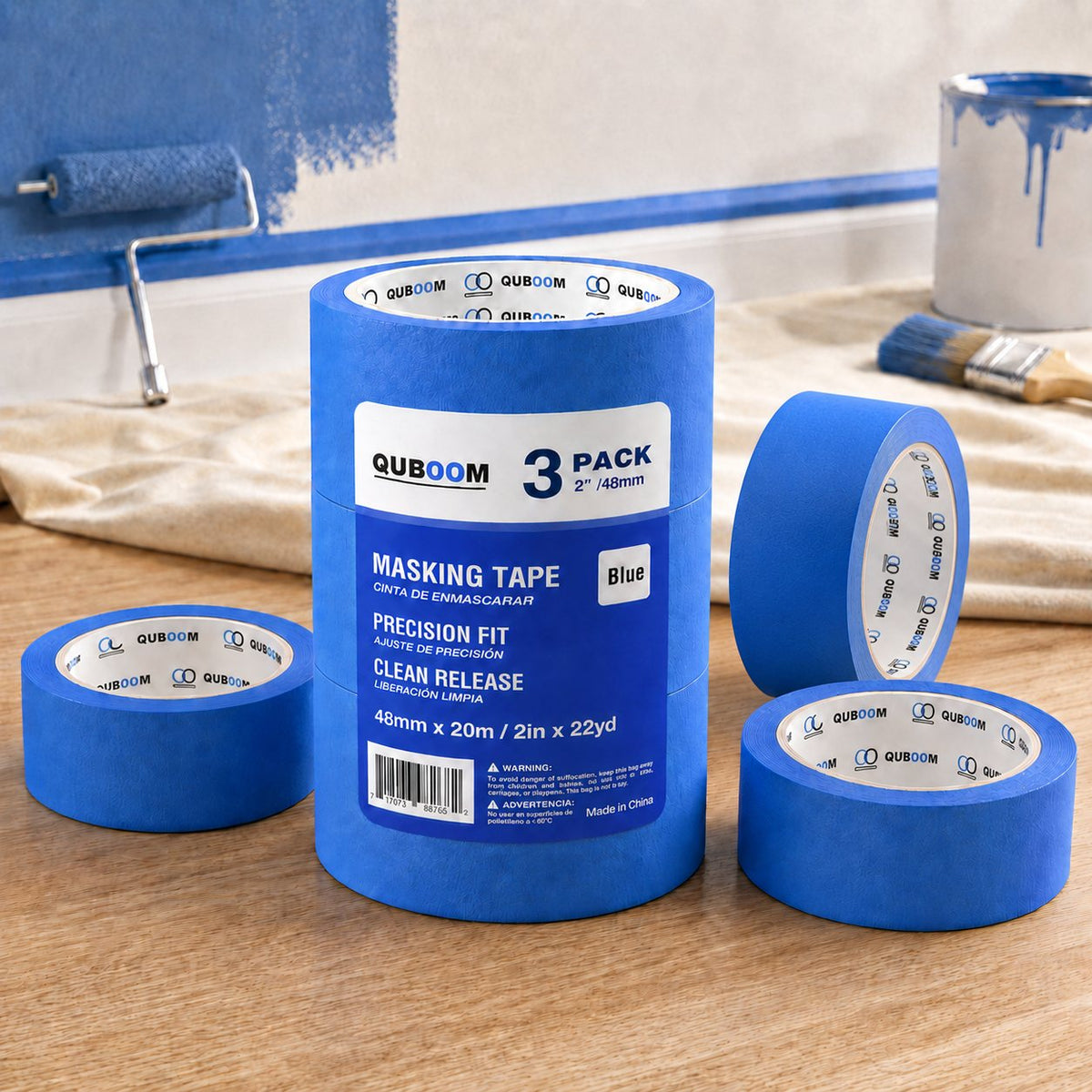 A 3-pack of blue tape and loose rolls on a drop cloth in a room being painted blue