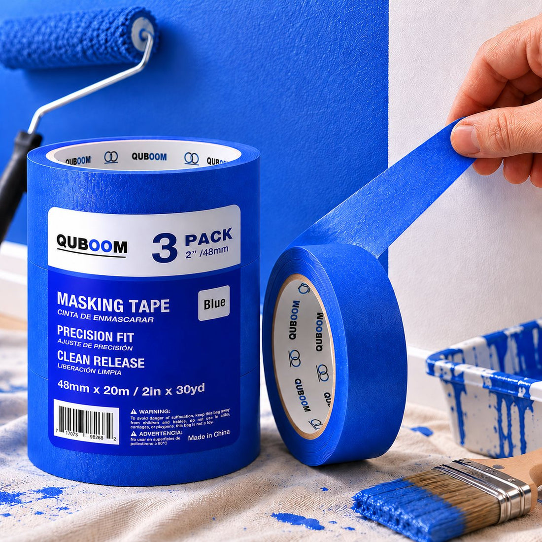 A hand peeling blue tape away from a freshly painted wall