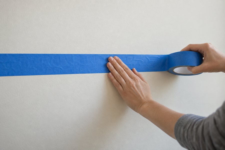 A hand laying blue tape along a wall