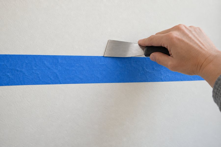 A putty knife pressing down the edge of the tape